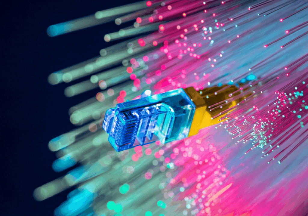 Macro sur un connecteur RJ45 bleu entouré de fibres optiques lumineuses aux couleurs bleu, vert et rose symbolisant la connectivité numérique haut débit